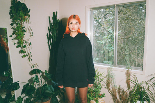A women stands in a room wearing an oversized black hoodie.